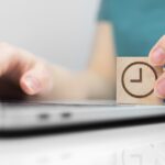 uma pessoa usando um notebook com um dado de madeira, simbolizando um relogio, para ilustrar o tempo medio de resposta de atendimento ao cliente